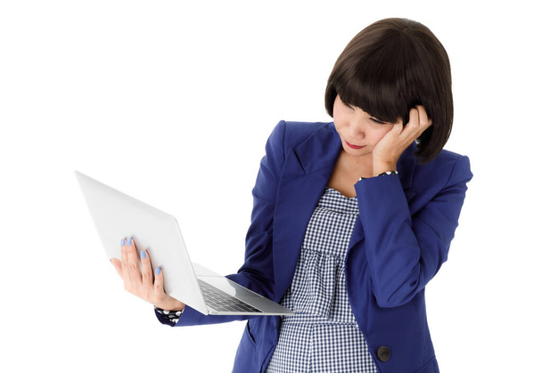 Усталая задумчивая молодая азиатка в стильном наряде, опираясь на руку и глядя на экран ноутбука во время работы в Интернете на белом фоне - Фото, изображение