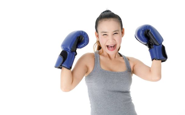 Victorious young Asian female fighter in blue boxing gloves raising hands and smiling happily while celebrating triumph against white background - Foto, afbeelding