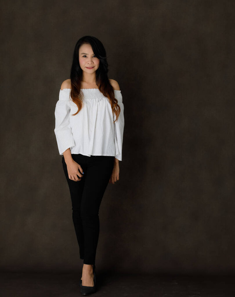 jong aziatisch zakenvrouw in elegant blazer kijken naar camera en glimlachen tegen donker grijs achtergrond - Foto, afbeelding