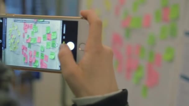 Close up of a girl with smartphone taking a reminder photo of a wall covered by post-it - Footage, Video