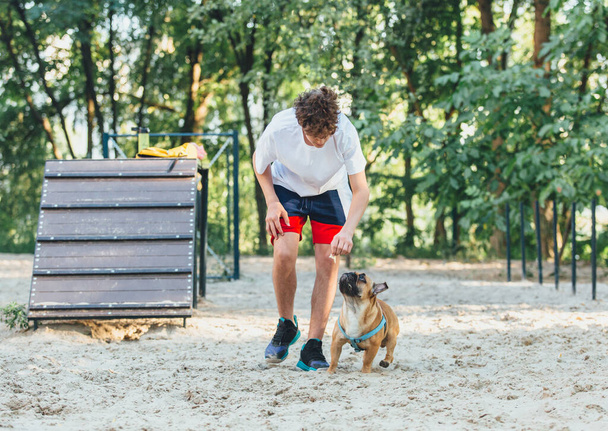 Der Besitzer einer französischen Bulldogge trainiert den Hund im Park. Hundetraining mit Jugendlichen und Bulldoggen im Freien. Stillleben, Liebe und Fürsorge für Haustiere, Tierfreundschaft. - Foto, Bild