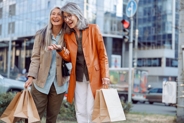 Melko kypsiä naisia, joilla on paljon ostoskasseja nauraa kaupungin kadulla - Valokuva, kuva