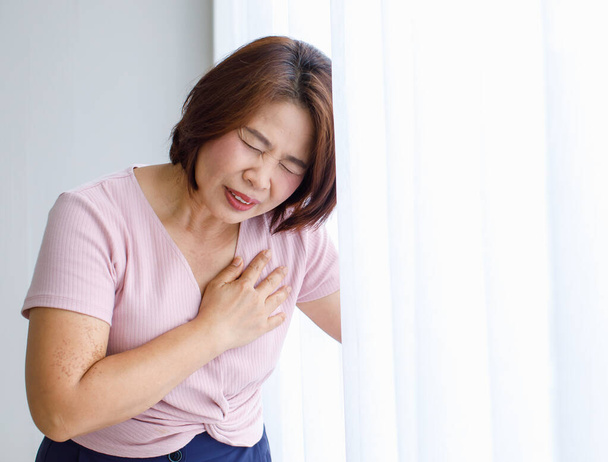 Woman leaning on wall with pain, suffer and distorted face and use hand to hold on the chest from heart disease. Concept of ST Elevated Myocardial Infarction. - Φωτογραφία, εικόνα
