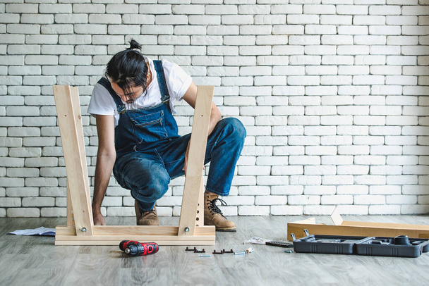機器やマニュアルで木製のテーブルを組み立て、便利屋として働くヒップスター若い男は、背景に白いレンガブロック壁と家庭の死とセルフサービスのための概念. - 写真・画像