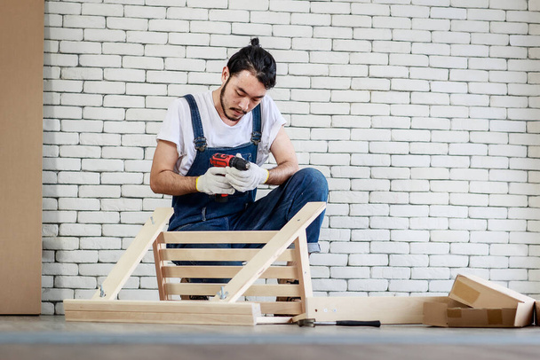Junger Mann asiatischer Hipster arbeitet als Heimwerker, montiert Holztisch mit Einrichtungsgegenständen, Konzept für Heimtextilien und Selbstbedienung im Büro gibt es eine weiße Ziegelwand. - Foto, Bild