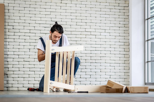 Junger Mann asiatischer Hipster arbeitet als Heimwerker, montiert Holztisch mit Einrichtungsgegenständen, Konzept für Heimtextilien und Selbstbedienung im Büro gibt es eine weiße Ziegelwand. - Foto, Bild