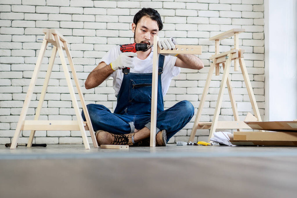 Jeune homme hipster asiatique travaillant comme bricoleur, assemblant une table en bois avec des équipements, concept de bricolage à domicile et self-service et passe-temps, - Photo, image