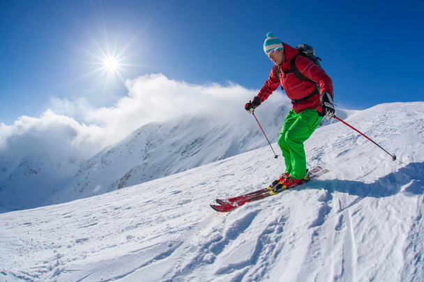 Esquiador esquiando cuesta abajo en las altas montañas durante el día soleado
 - Foto, imagen