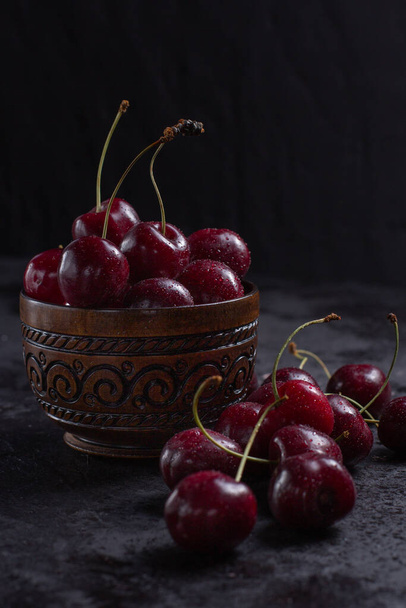 Organic juicy cherry in a bowl with water drops on berries on dark background. Close-up photo, low key.  - Zdjęcie, obraz
