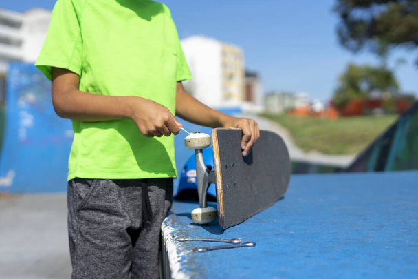 Unrecognizable boy repairs the wheel of his skateboard after using it inside the skateboarders park. - Fotoğraf, Görsel
