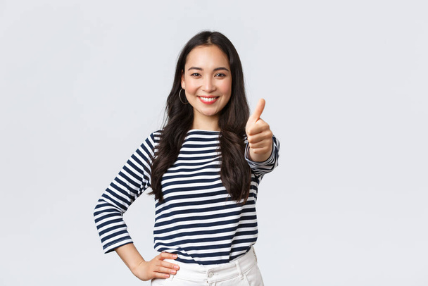 Lifestyle, beauty and fashion, people emotions concept. Cheerful cute asian girl thumb-up in approval, wink encouraging and smiling, praising nice job, say well played as congratulate with win - Photo, Image