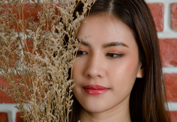 Close up de jovem bonito rosto feminino asiático atraente modelo com ramo de flor contra fundo de parede de tijolo laranja. - Foto, Imagem