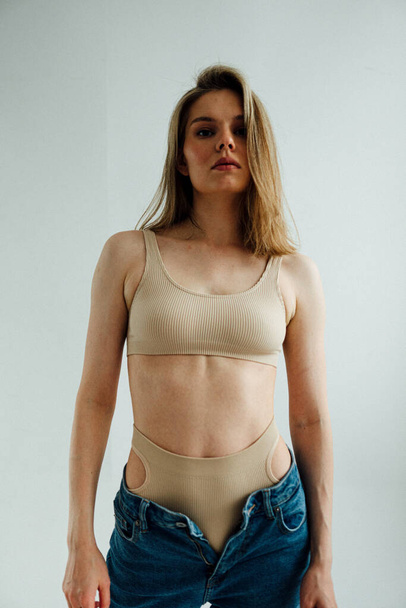 schönes Mädchen mit athletischem Körper in sportlicher Dessous und Jeans posiert im hellen Studio  - Foto, Bild