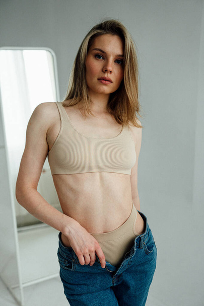menina bonita com corpo atlético vestindo lingerie esportiva e jeans posando em estúdio de luz  - Foto, Imagem