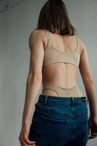 задний вид женской модели со спортивным телом в спортивном нижнем белье и джинсах, позирующих в легкой студии  - Фото, изображение