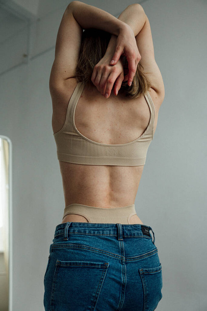 Rückansicht des weiblichen Modells mit athletischem Körper in sportlicher Dessous und Jeans posiert im hellen Studio  - Foto, Bild