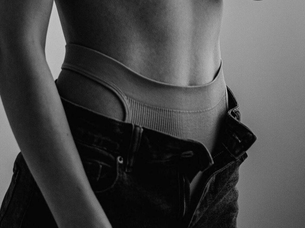 menina bonita nua com corpo atlético vestindo lingerie esportiva e jeans posando no estúdio de luz  - Foto, Imagem