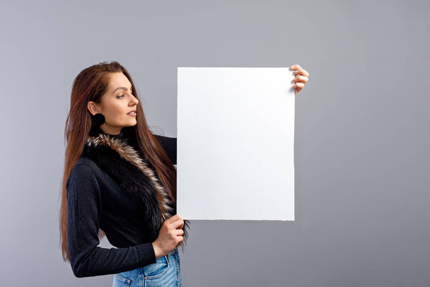 emotional young teenager woman showing blank signboard with copy space, isolated on gray - Photo, image