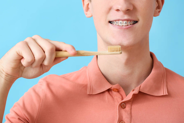 Schöner Mann mit Zahnspange und Zahnbürste auf farbigem Hintergrund, Nahaufnahme - Foto, Bild