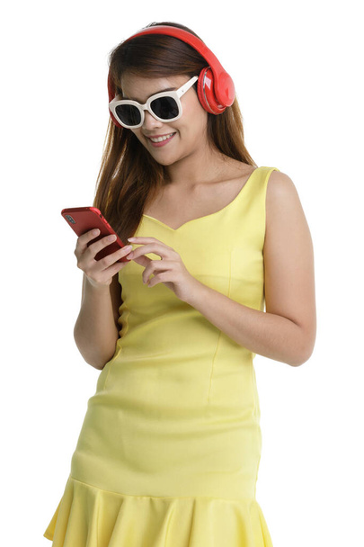 Izolovaný portrét zblízka záběr asijské šťastný žena teenager nosit velké červené sluchátka stojí s úsměvem pohled na obrazovce držet smartphone v rukou poslech hudby a tance. - Fotografie, Obrázek