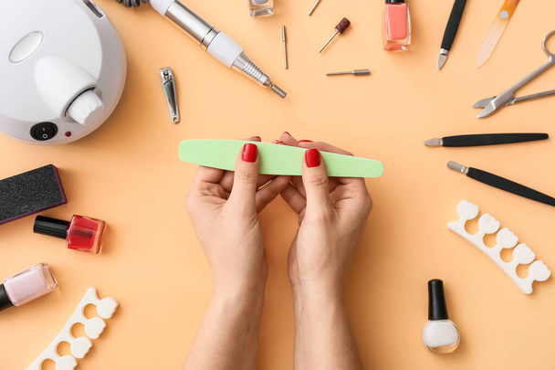 Manos femeninas con lima de uñas y herramientas para manicura sobre fondo de color - Foto, imagen