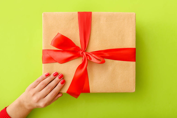 Γυναικείο χέρι με όμορφο μανικιούρ και κουτί δώρου στο φόντο χρώμα - Φωτογραφία, εικόνα