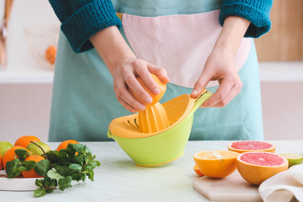 Mulher espremendo laranja para suco na mesa na cozinha - Foto, Imagem