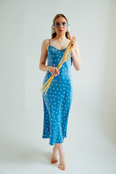stylish girl in blue polka dot dress and sunglasses with kerchief holding spikelets of wheat and posing in studio - Photo, Image