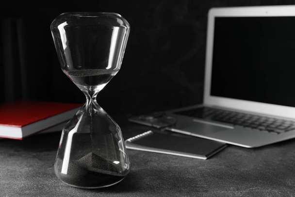 Stylish hourglass and laptop on dark table in office. Deadline concept - Valokuva, kuva