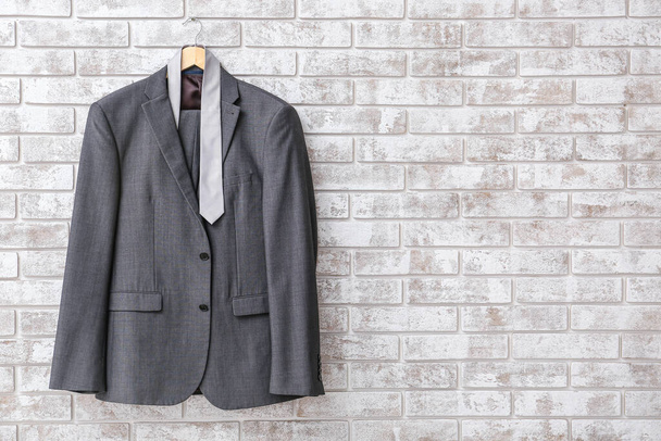 Hanger with stylish suit and necktie hanging on brick wall - Photo, Image