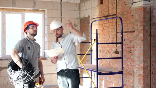 En el centro de la sala de ser renovado, dos trabajadores de la construcción en cascos están de pie y discutiendo. - Imágenes, Vídeo