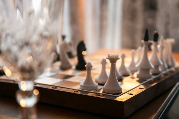 Стекло и игровая доска с шахматными фигурами на столе, крупный план - Фото, изображение