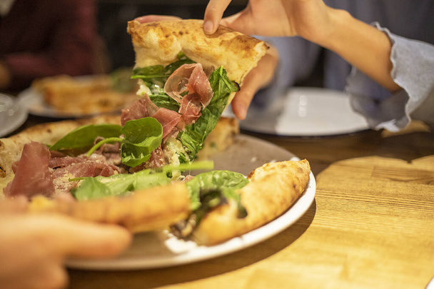 tomar um pedaço quente de pizza com as mãos com espinafre prosciutto e parmesão close-up, horizontal - Foto, Imagem