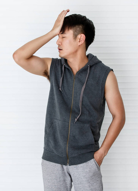 Young asian man wearing sleeveless t-shirt gray sportswear holding hand forehead show error, failure in white background - Photo, Image