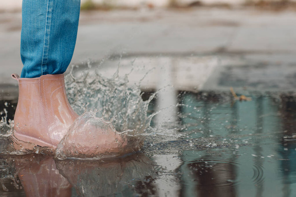 Woman wearing rain rubber boots walking running and jumping into puddle with water splash and drops in autumn rain - Foto, immagini