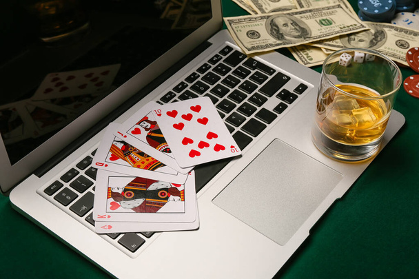 Laptop, cartas de baralho para pôquer, notas de dólar e copo de bebida na mesa do cassino - Foto, Imagem