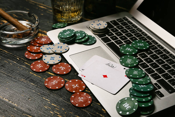 Laptop, poker chips and playing cards on dark wooden background - Photo, Image