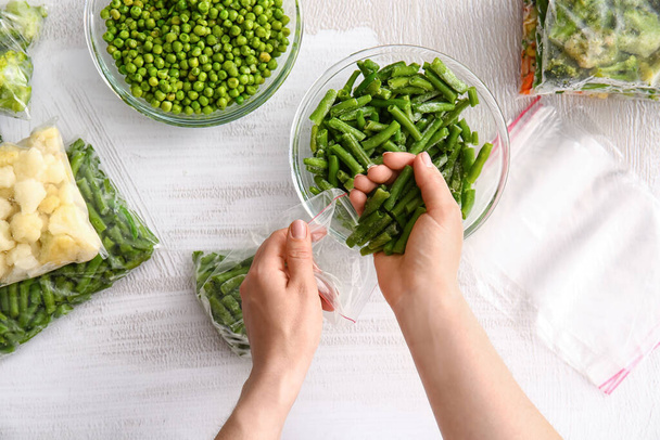 Woman putting frozen green beans in plastic bag on light background - Photo, Image