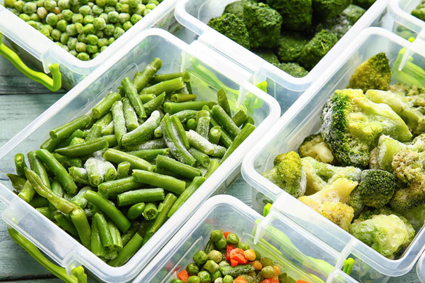 Пластиковые контейнеры с различными замороженными овощами на фоне цвета дерева - Фото, изображение