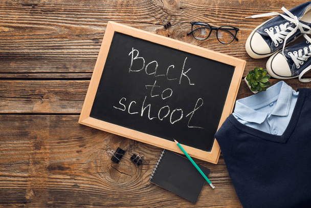 Chalkboard with text BACK TO SCHOOL, uniform, shoes, eyeglasses and stationery on wooden background - Photo, Image