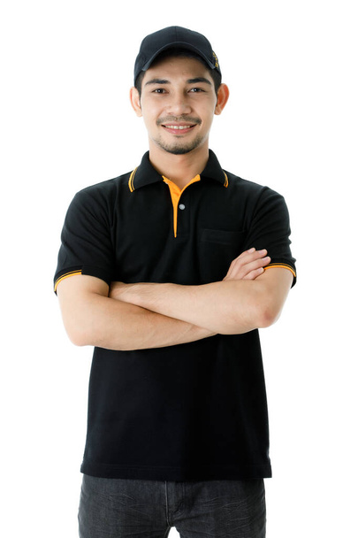 Confident Asian delivery man smiles and looks at camera with crossed arms. Studio medium shot portrait of courier guy in black uniform on isolated white background. E-commerce business concept - Photo, Image