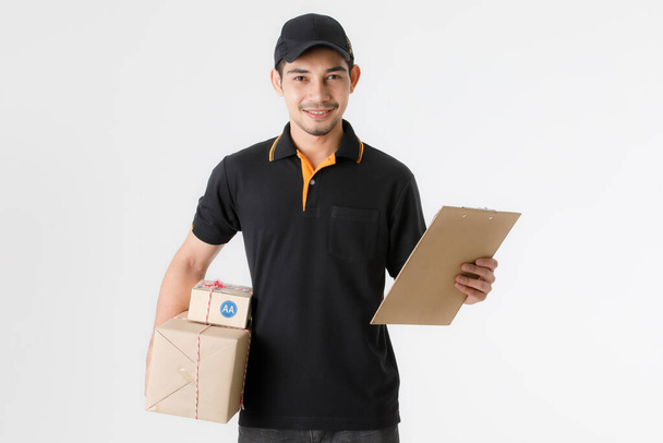 Atrakcyjny azjatycki dostawca trzymać paczkę w prawej ręce i arkusz dostaw w lewej ręce. Studio portret kuriera w czarnym mundurze na białym tle. Koncepcja handlu elektronicznego - Zdjęcie, obraz