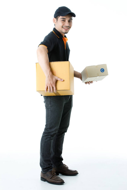 Radosny azjatycki dostawca trzyma paczki w każdej ręce, uśmiech do kamery. Studio portret kuriera w czarnym mundurze na białym tle. Koncepcja handlu elektronicznego - Zdjęcie, obraz