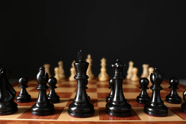 Chess pieces on wooden board against black background - 写真・画像