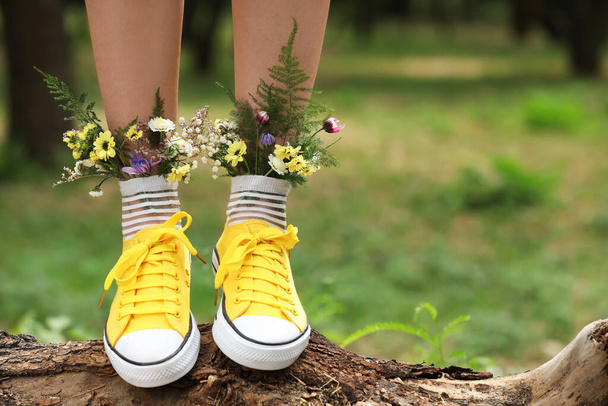 Woman standing on log with flowers in socks outdoors, closeup. Space for text - Zdjęcie, obraz