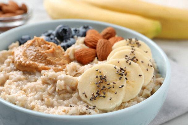Tasty oatmeal porridge with toppings in bowl on table, closeup - Фото, зображення