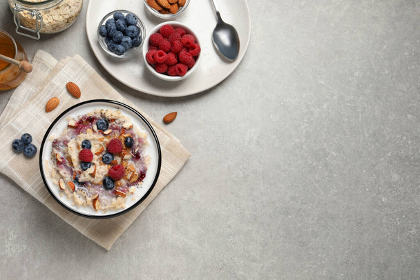 Tasty oatmeal porridge with toppings served on grey table, flat lay. Space for text - Foto, afbeelding