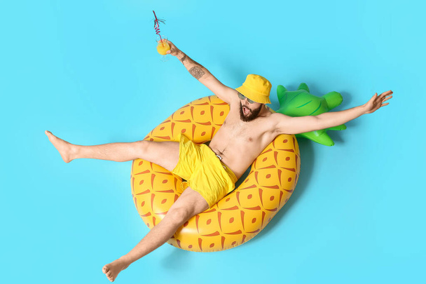 Young man with inflatable ring drinking cocktail on color background - Foto, imagen