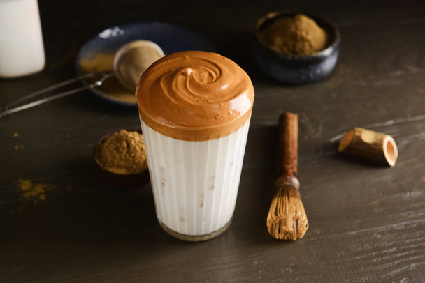 Glass of tasty dalgona hojicha latte and chasen on dark wooden background - Foto, immagini