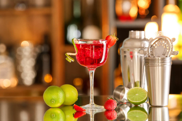 Glass of tasty cosmopolitan cocktail with strawberries and lime on table in bar - Photo, Image